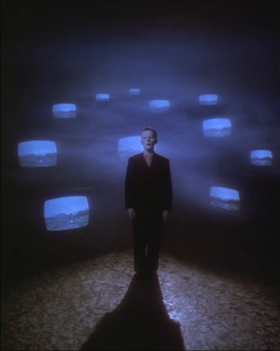 A solitary figure among blue television screens in a dark room